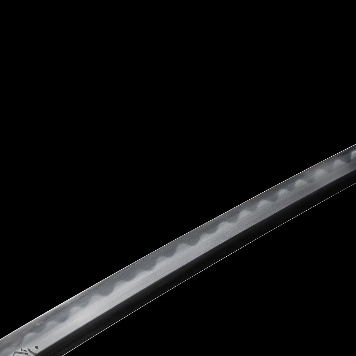 Close-up detail of a Japanese katana blade against a deep black background, polished steel surface showing a visible wavy hamon line along the cutting edge, smooth reflective finish with subtle tonal contrast between edge and body, no scabbard or mount visible, emphasis on blade curvature, edge geometry, and traditional differential hardening pattern.
