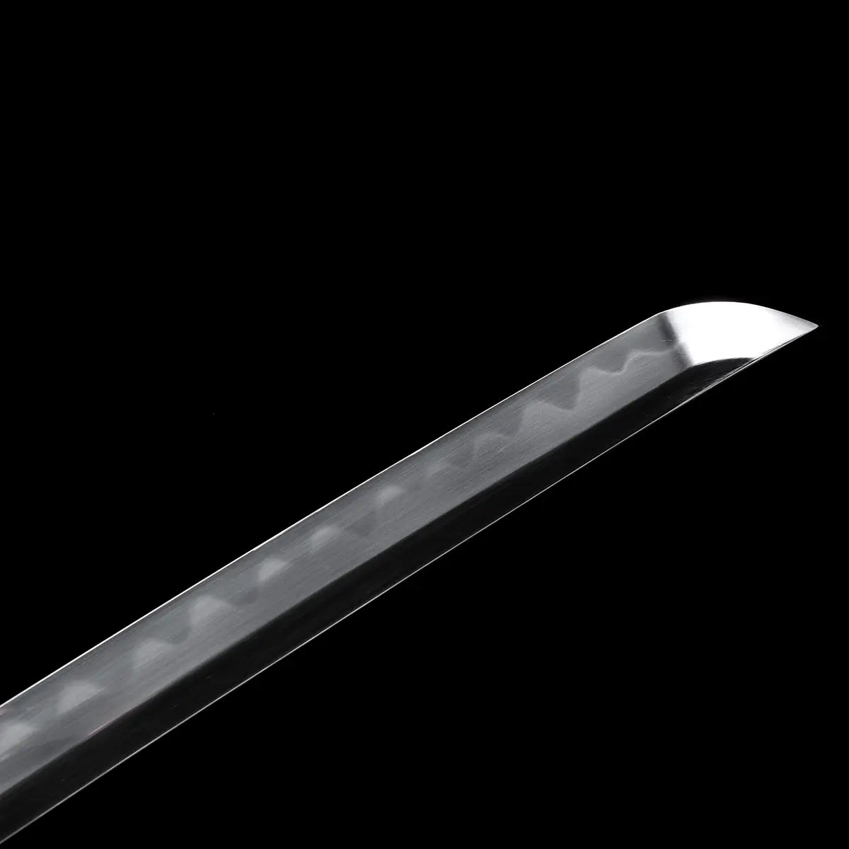 Close-up detail of a Japanese katana blade tip against a deep black background, polished steel kissaki with a clean reflective finish, visible wavy hamon line running toward the tip, sharp cutting edge and defined curvature, no scabbard or mount present, emphasis on blade geometry, tip profile, and differential hardening pattern.
