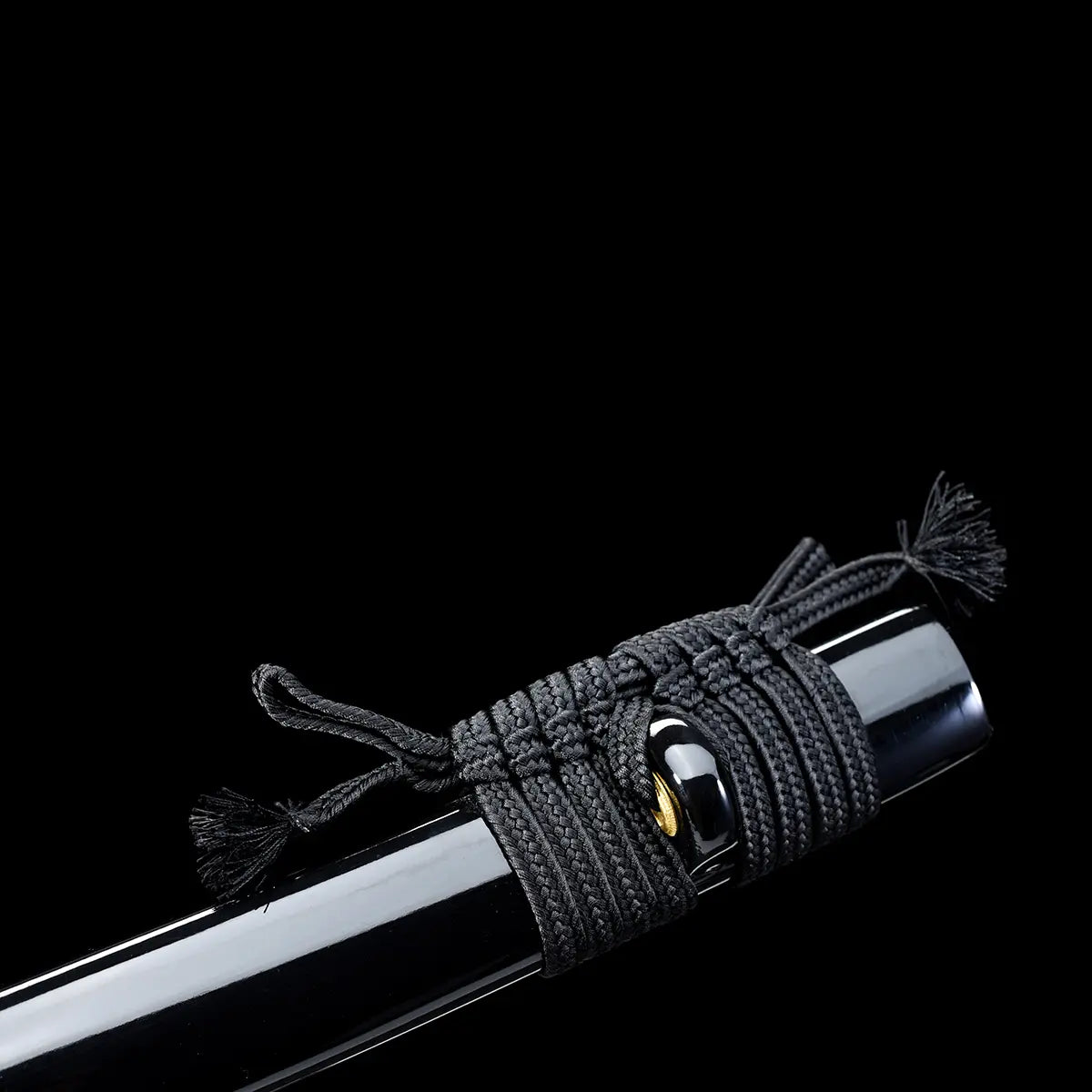 Close-up detail of a Japanese katana scabbard against a deep black background, glossy black lacquered wooden saya wrapped with a black braided sageo cord, visible knot and tassels, smooth reflective surface of the scabbard, gold-colored kurigata ring partially visible, focus on traditional scabbard finish and cord texture.
