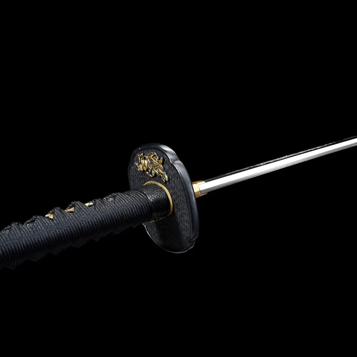 Angled close-up view of a Japanese katana against a deep black background, black textured tsuba with raised golden relief figure, gold-colored brass habaki fitted at the base of the polished steel blade, black tsuka wrapped tightly with black cord over ray skin, partial view of the straight blade section extending forward, emphasis on traditional fittings, materials, and metal finishes.
