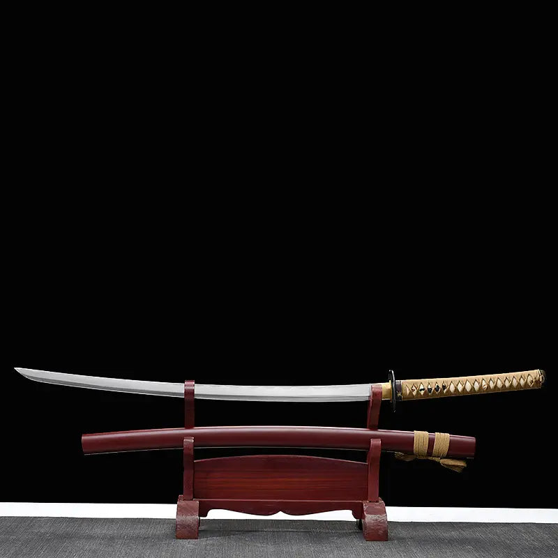 Katana Himura Kenshin Sakabato a lame inversee expose sur un support en bois rouge devant un fond noir, sabre degainne avec lame courbee en acier, fourreau rouge laque pose sous le katana, manche beige tresse avec peau de raie et garde noire ronde.
