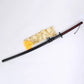 Photo du katana Ichigo Kurosaki Tensa Zangetsu version classique, réplique Bankai de Bleach en acier carbone 1045, avec fourreau noir mat, poignée noire et losanges rouges, posé sur un fond blanc avec une housse décorative dorée.