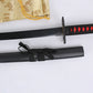 Vue rapprochée du katana Ichigo Kurosaki Tensa Zangetsu version classique, réplique Bankai de Bleach en acier carbone 1045, montrant la lame noire partiellement dégainée, le fourreau noir mat avec sageo noué, la poignée noire tressée à losanges rouges et une housse dorée en arrière-plan, sur fond blanc.