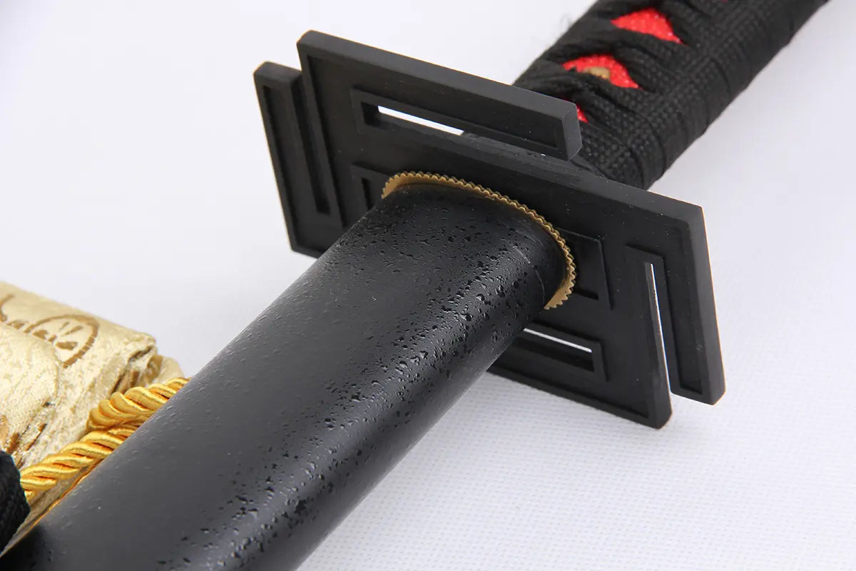 Détail rapproché de la garde noire rectangulaire du katana Ichigo Kurosaki Tensa Zangetsu version classique, réplique Bankai de Bleach en acier carbone 1045, avec poignée noire tressée et losanges rouges, fourreau noir mat et housse dorée en arrière-plan.