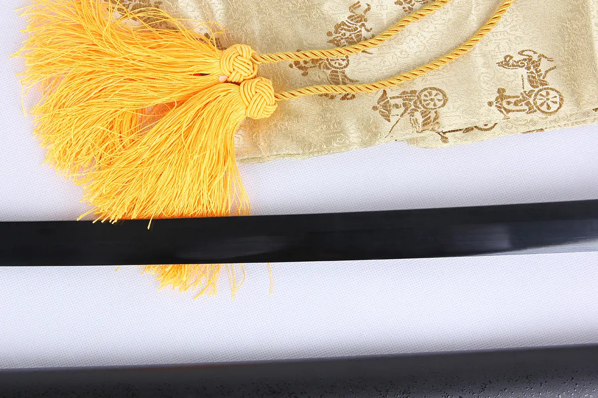Détail de la lame noire du katana Ichigo Kurosaki Tensa Zangetsu version classique, réplique Bankai de Bleach en acier carbone 1045, accompagnée d’une housse décorative dorée à motifs et cordon jaune, posée sur fond blanc.