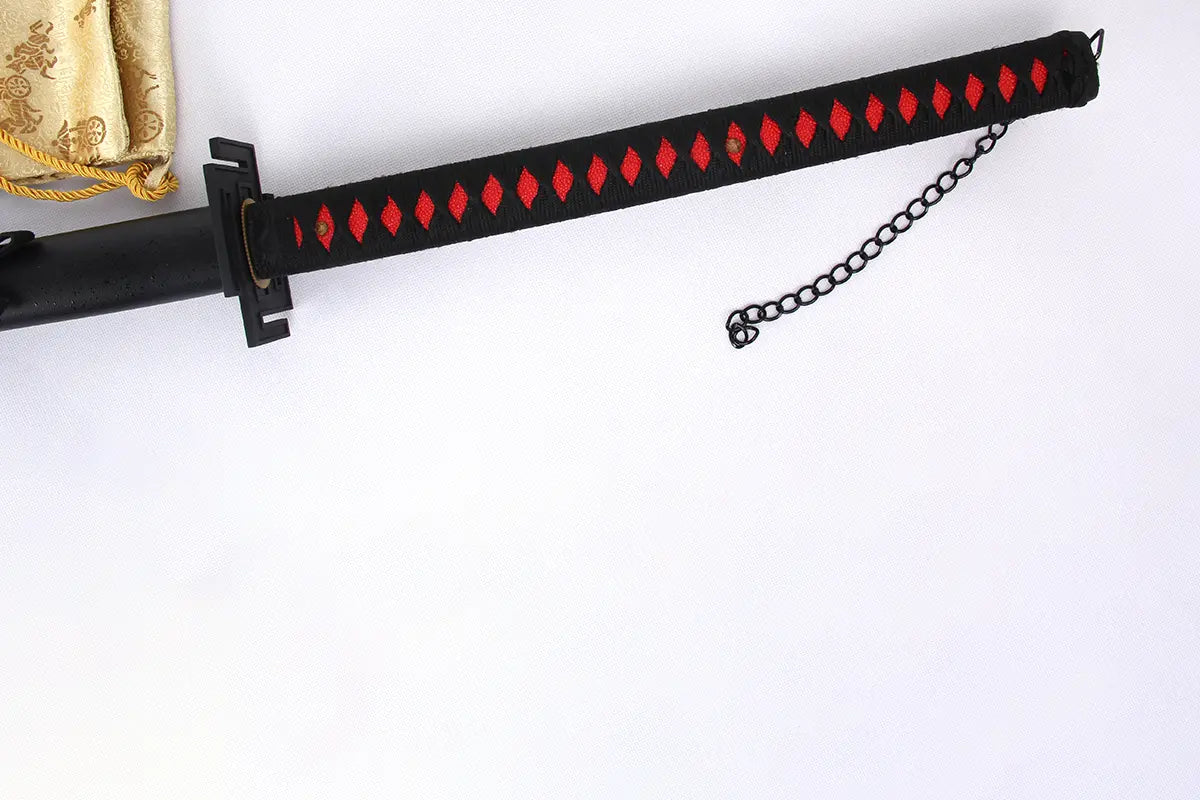 Gros plan sur la poignée noire tressée du katana Ichigo Kurosaki Tensa Zangetsu version classique, réplique Bankai de Bleach en acier carbone 1045, avec losanges rouges, garde noire rectangulaire et chaînette métallique, posé sur fond blanc avec housse dorée en arrière-plan.