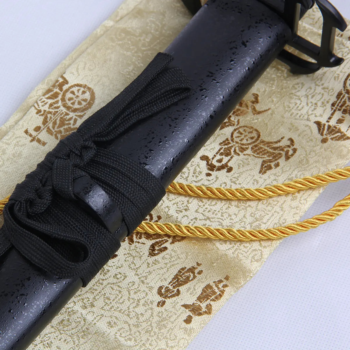 Détail du fourreau noir mat du katana Ichigo Kurosaki Tensa Zangetsu version stylisée, réplique collector Bleach, avec cordon noir soigneusement noué, posé sur tissu doré brodé de motifs traditionnels japonais.