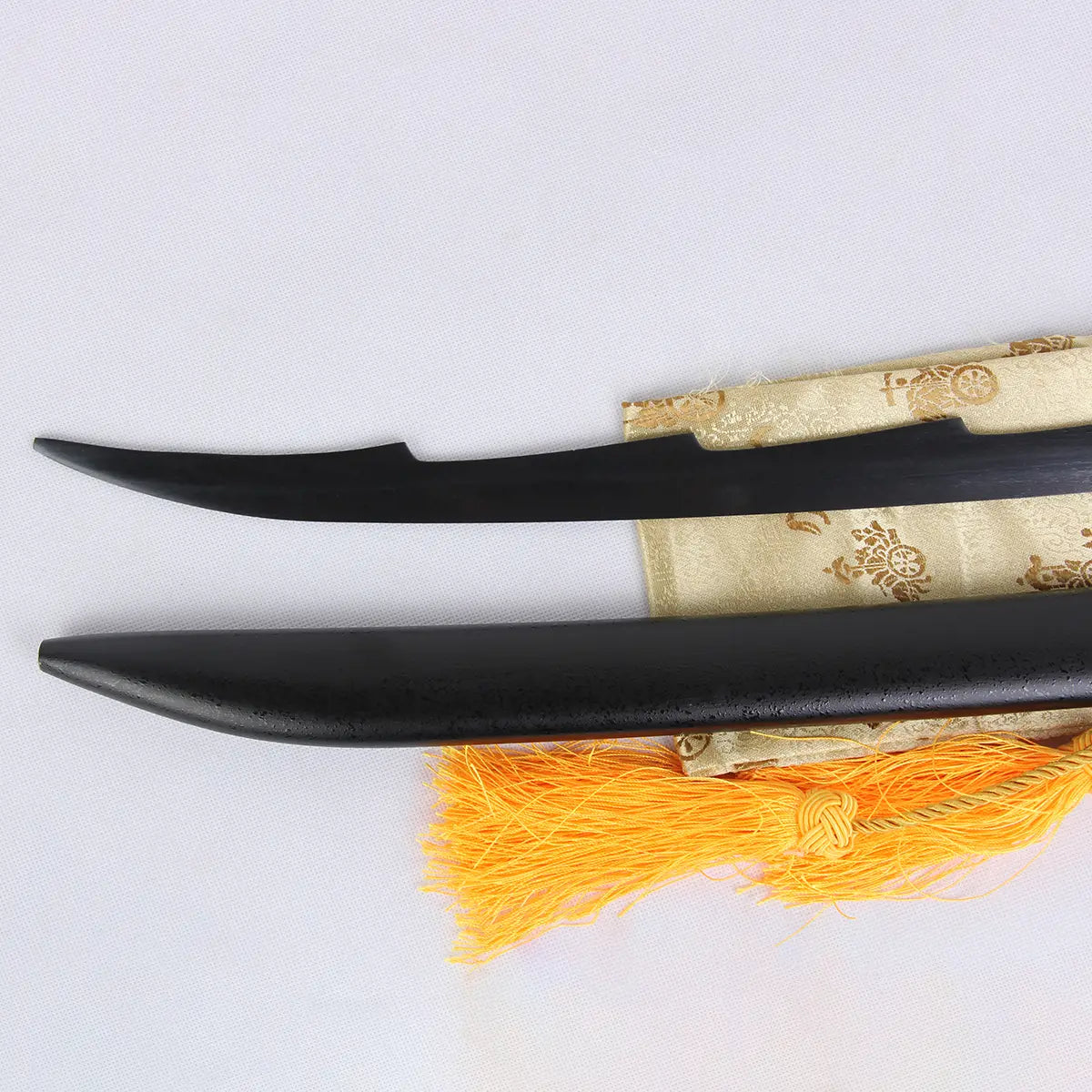 Détail de la lame noire stylisée du katana Ichigo Kurosaki Tensa Zangetsu et de son fourreau assorti, réplique collector Bleach, posés sur un tissu doré avec franges orange en fond clair.