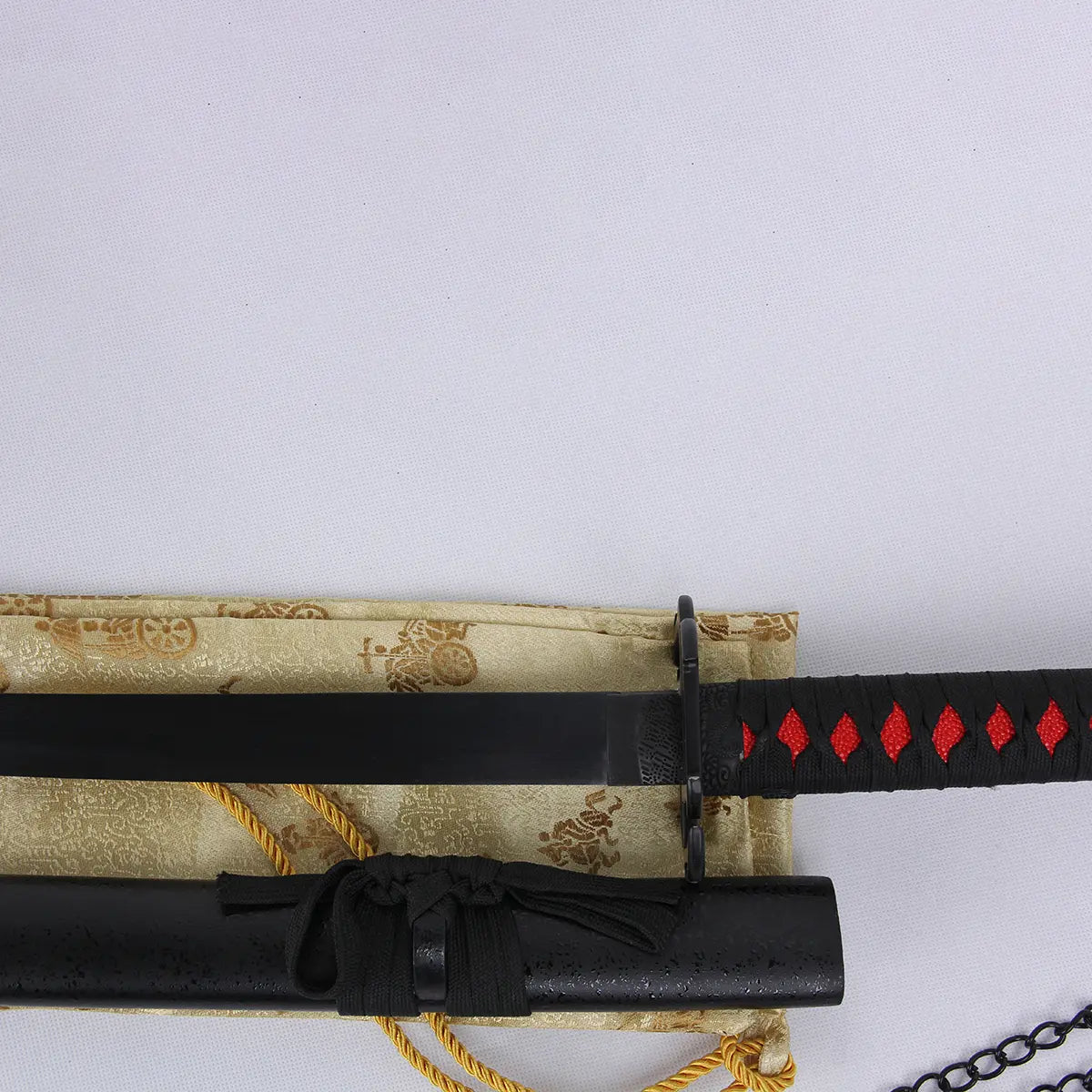 Vue rapprochée du katana Ichigo Kurosaki Tensa Zangetsu version stylisée, réplique collector Bleach, montrant la lame noire, la garde carrée et la poignée tressée noire avec motifs rouges, posé sur tissu doré brodé japonais.