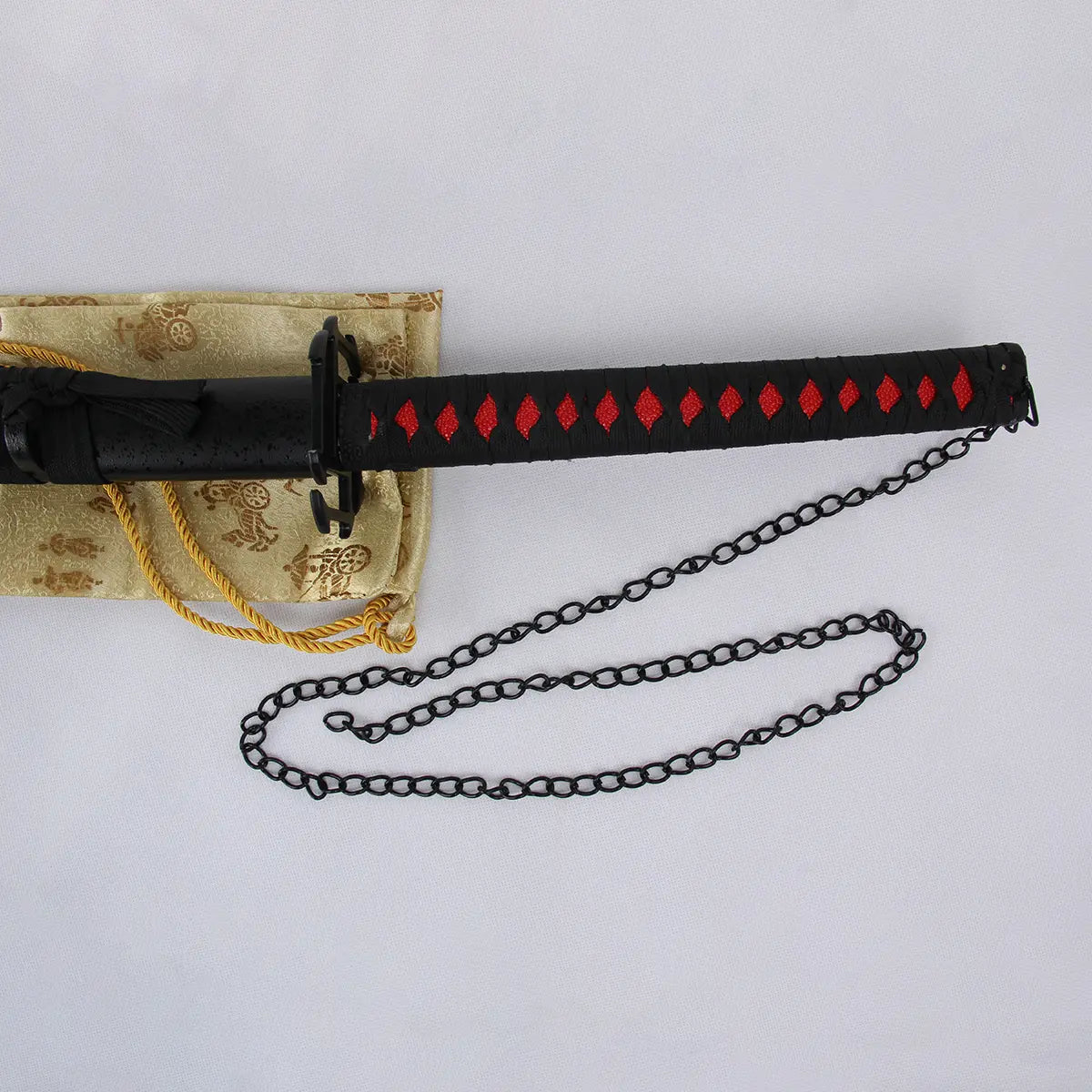 Poignée noire tressée avec motifs rouges du katana Ichigo Kurosaki Tensa Zangetsu version stylisée, réplique collector Bleach, équipée d’une chaîne noire décorative, posée sur un tissu doré avec motifs traditionnels japonais.