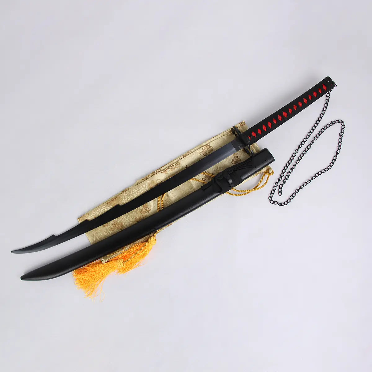 Katana Ichigo Kurosaki Tensa Zangetsu version stylisée, réplique collector Bleach en acier carbone, lame noire avec fourreau assorti et poignée noire tressée rouge, chaîne décorative noire, posé sur tissu doré avec franges orange.