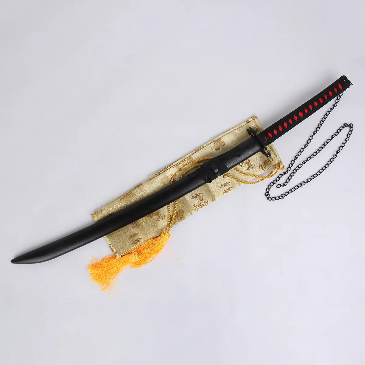 Katana Ichigo Kurosaki Tensa Zangetsu version stylisée, réplique collector Bleach avec fourreau noir mat et poignée noire tressée rouge, chaîne décorative, présenté sur un tissu doré avec franges orange en fond clair.