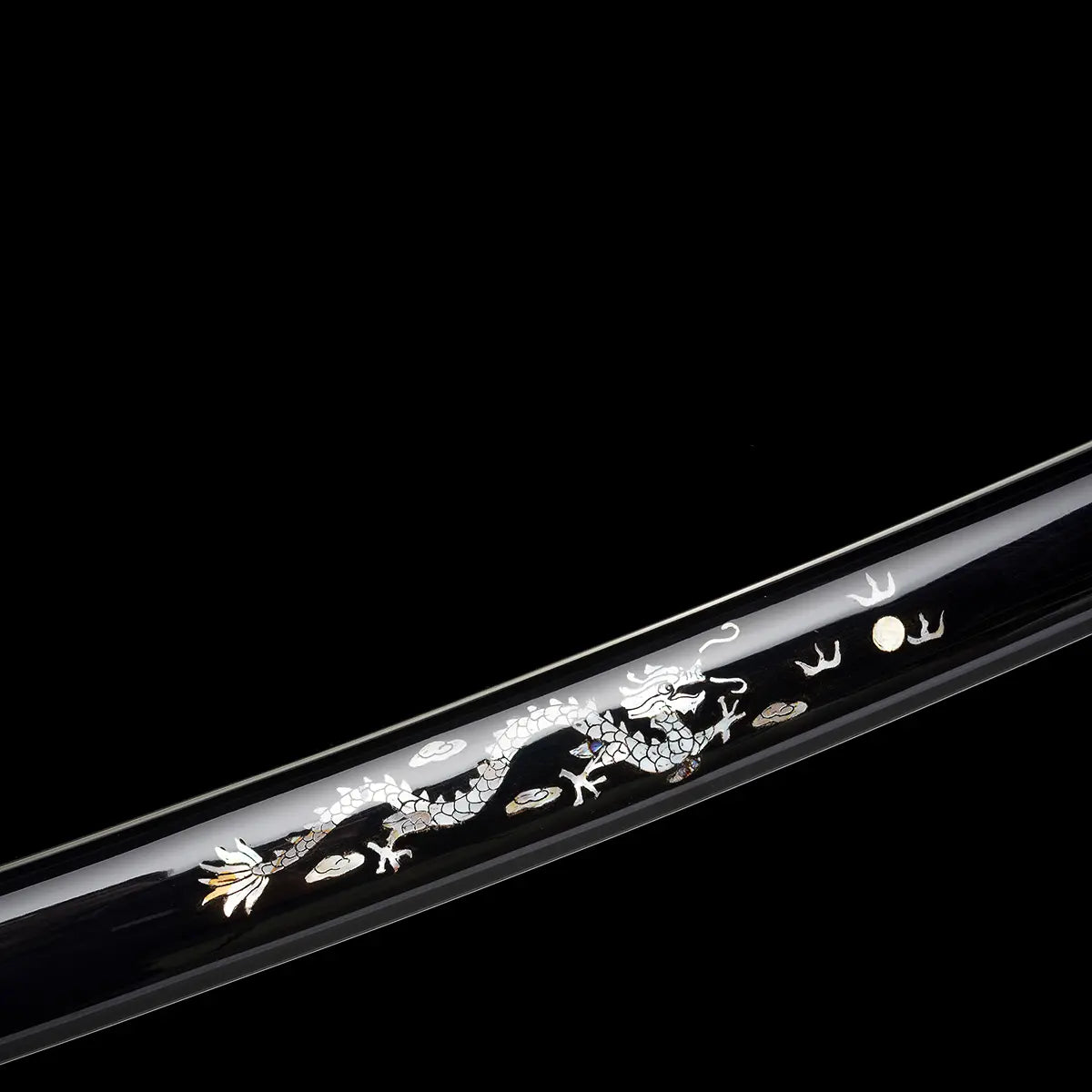 Détail du fourreau du katana japonais artisanal Ryū no Kiba sur fond noir uni, saya noir laqué orné d’une incrustation décorative représentant un dragon argenté avec éléments dorés, finition brillante et lisse du fourreau, motif visible sans lame ni support apparent.

