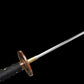 Gros plan sur la poignée du katana japonais artisanal Ryū no Kiba sur fond noir uni, tsuka enveloppée de cordage noir avec losanges blancs en peau de raie, garde tsuba ronde en métal patiné avec motifs décoratifs dorés, habaki doré visible, lame partiellement floutée en arrière-plan sans fourreau ni support.
