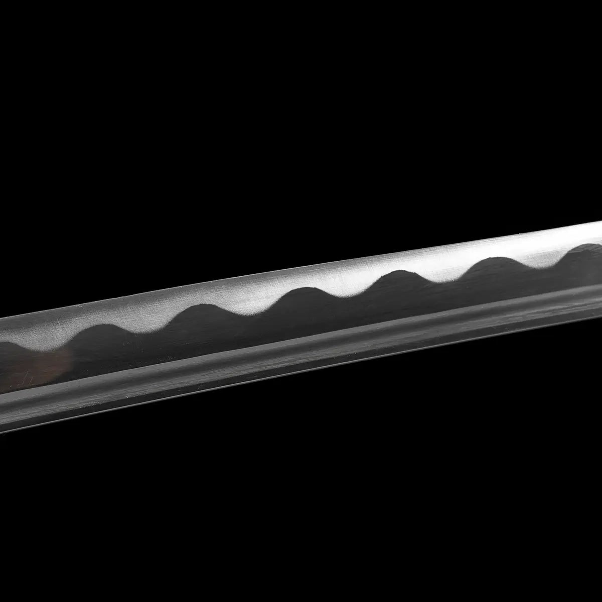 Close-up detail of the polished steel blade of the Japanese artisanal katana Hana no Yuki on a solid black background, showing the wavy hamon pattern along the cutting edge, smooth blade curvature, fine surface finish, and the bo-hi groove running parallel to the spine
