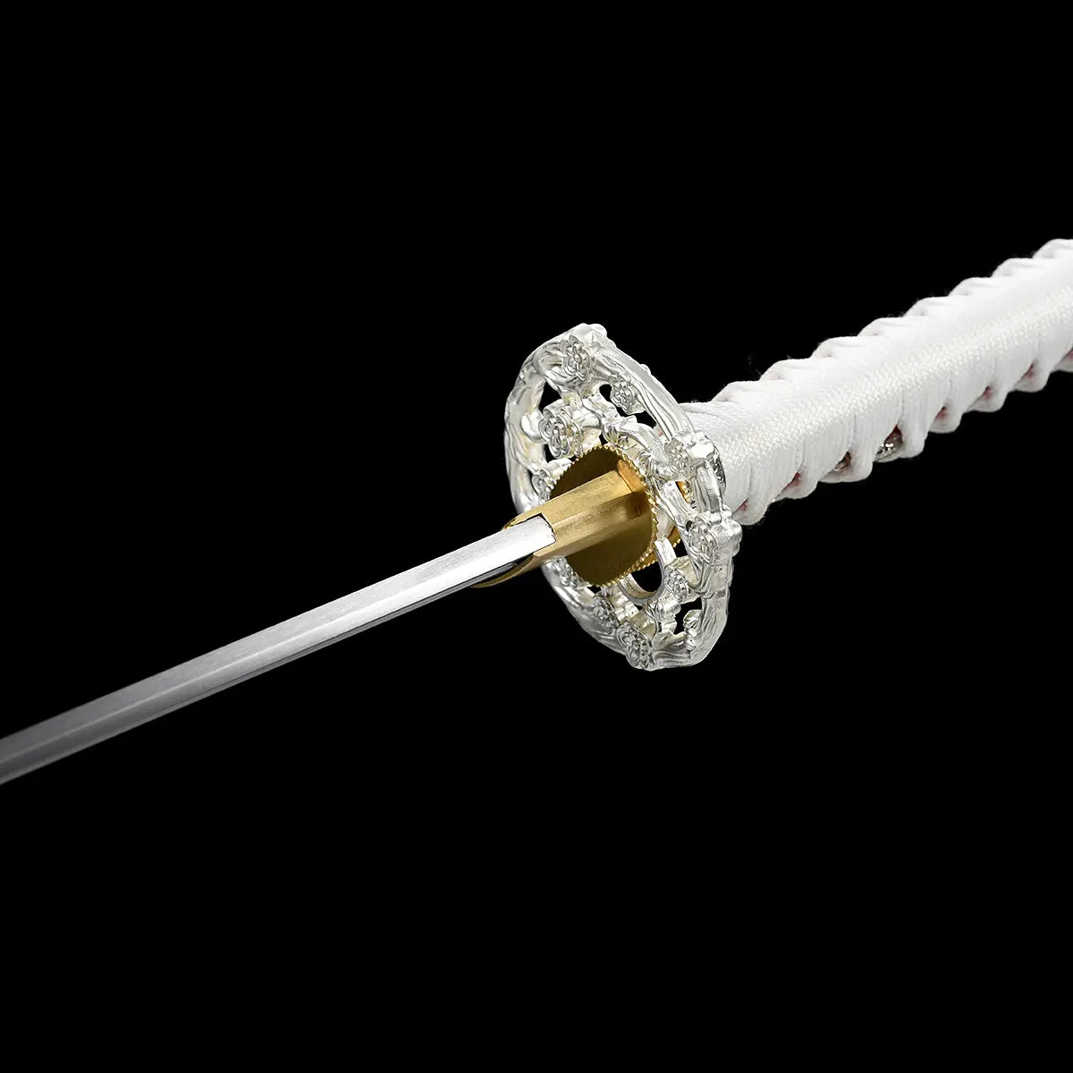 Rear close-up view of the Japanese artisanal katana Hana no Yuki on a solid black background, showing the back side of the ornate silver floral openwork tsuba, the gold-colored brass habaki fitted around the blade base, part of the polished steel blade spine, and the white tsuka wrapped in white ray skin with red ito diamond pattern
