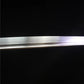 Close-up view of the polished carbon steel blade of the Japanese artisanal katana Mushin, showing smooth linear grain from hand polishing, clean edge line without visible hamon, subtle light reflection along the curvature, deep black background emphasizing the minimalist shirasaya blade finish
