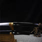 Close-up view of the Japanese artisanal katana Mushin in shirasaya mount, showing the black lacquered wooden saya aligned with the polished steel blade, brass habaki visible near the junction, smooth reflective surface, dark black background and grey fabric base, minimalist and traditional Japanese sword presentation
