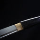 Close-up detail of the Japanese artisanal katana Mushin showing the brass habaki fitted between the polished carbon steel blade and the black lacquered wooden saya, clean junction and smooth surfaces, minimalist shirasaya construction highlighted against a deep black background
