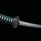 Détail de la lame du katana japonais artisanal Seiryū no Tachi photographié sur fond noir uni. La base de la lame courbe en acier carbone est visible avec un hamon réel ondulé et un polissage satiné. La tsuba métallique finement sculptée à motifs floraux entoure un habaki de couleur laiton, tandis que le manche est recouvert d’un tsuka-ito vert foncé laissant apparaître une same blanche en losanges réguliers.

