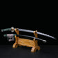 Katana japonais artisanal Seiryū no Tachi photographié sur fond noir, présenté sur un support en bois sculpté. La lame courbe en acier carbone est exposée hors du fourreau, montrant un hamon réel ondulé sur toute la longueur. Le fourreau noir laqué repose sur le support inférieur. Le manche est recouvert d’un tsuka-ito vert foncé avec same blanche apparente, et les montures métalliques traditionnelles sont visibles sur l’ensemble du sabre.
