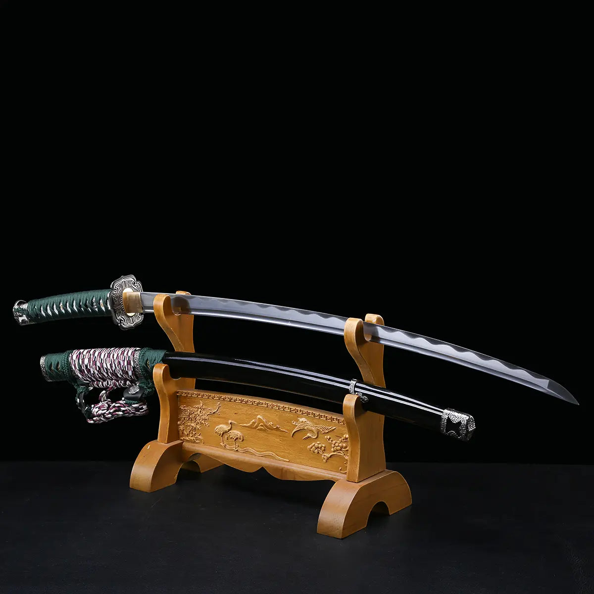 Katana japonais artisanal Seiryū no Tachi photographié sur fond noir, présenté sur un support en bois sculpté. La lame courbe en acier carbone est exposée hors du fourreau, montrant un hamon réel ondulé sur toute la longueur. Le fourreau noir laqué repose sur le support inférieur. Le manche est recouvert d’un tsuka-ito vert foncé avec same blanche apparente, et les montures métalliques traditionnelles sont visibles sur l’ensemble du sabre.
