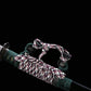 Détail du sageo du katana japonais artisanal Seiryū no Tachi photographié sur fond noir uni. Le fourreau noir laqué est partiellement visible, avec un sageo épais tressé aux couleurs vert foncé, blanc et pourpre, noué de manière traditionnelle. Les attaches métalliques du sageo et les finitions du fourreau sont visibles, montrant un assemblage soigné et une texture textile dense.
