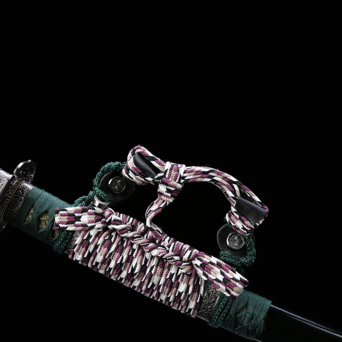 Détail du sageo du katana japonais artisanal Seiryū no Tachi photographié sur fond noir uni. Le fourreau noir laqué est partiellement visible, avec un sageo épais tressé aux couleurs vert foncé, blanc et pourpre, noué de manière traditionnelle. Les attaches métalliques du sageo et les finitions du fourreau sont visibles, montrant un assemblage soigné et une texture textile dense.
