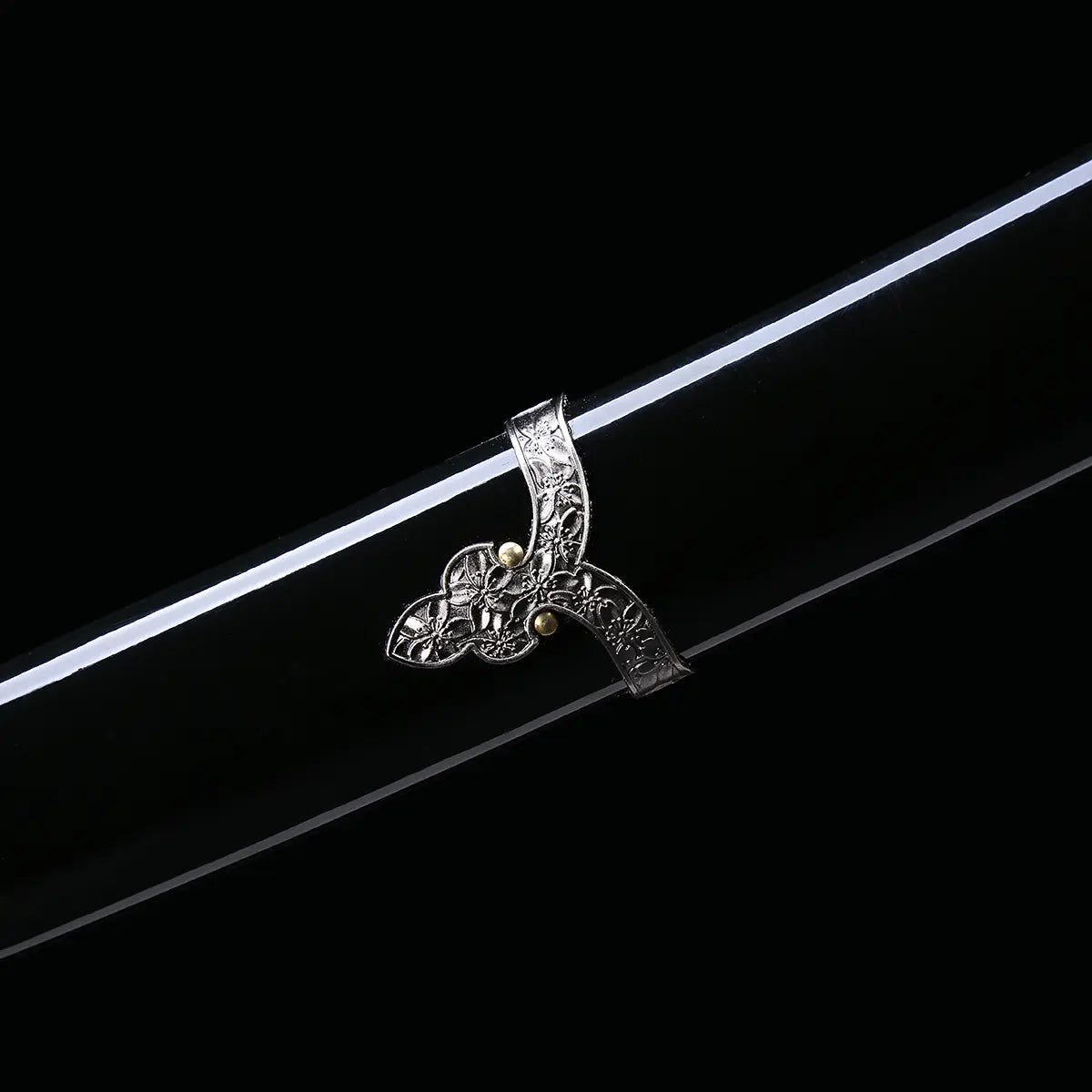 Détail du système d’attache (ashi) du fourreau du katana japonais artisanal Seiryū no Tachi photographié sur fond noir uni. Le saya noir laqué est visible avec une monture métallique décorative finement sculptée, fixée le long du fourreau pour le port traditionnel du tachi. Les éléments métalliques argentés présentent des motifs floraux en relief, avec des rivets visibles, soulignant la courbure et la finition soignée du fourreau.
