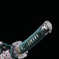 Détail du manche du katana japonais artisanal Seiryū no Tachi photographié sur fond noir uni. Le tsuka est recouvert d’un tsuka-ito vert foncé tressé serré, laissant apparaître une same blanche en losanges. Le pommeau (kashira) et la garde (tsuba) en métal sculpté sont visibles, avec des finitions argentées et un assemblage traditionnel japonais.
