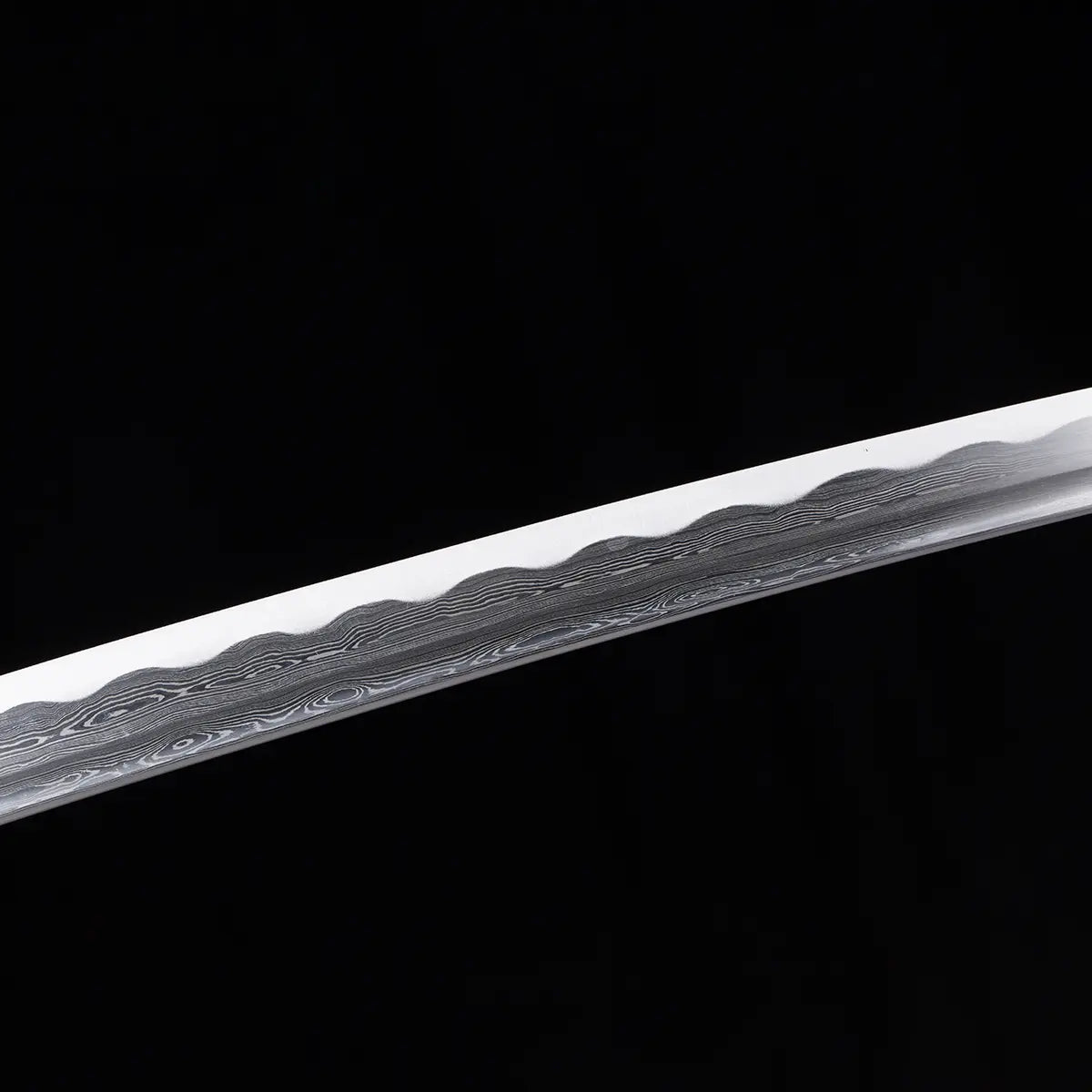 Gros plan de la lame du katana japonais Date Masamune, acier plié damassé à 880 couches avec hamon ondulé bien marqué, photographié sur fond noir pour mettre en valeur les motifs de l’acier – katana artisanal de collection Blade Bushido.