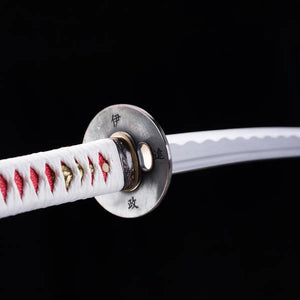 Vue rapprochée du katana japonais Date Masamune, garde (tsuba) en métal gravée de caractères japonais, lame pliée avec hamon ondulé, poignée blanche au tressage rouge et ornements dorés, photographié sur fond noir – katana de collection Blade Bushido.