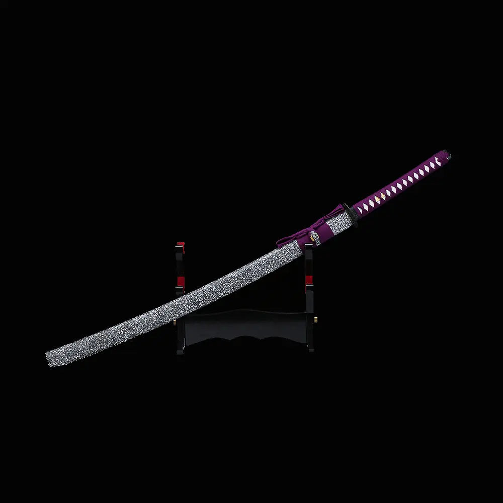 Katana japonais artisanal Murasaki no Kage photographié sur fond noir avec le fourreau noir laqué à éclaboussures blanches posé en diagonale sur un support en bois, poignée violette tressée avec peau de raie blanche visible et cordon sageo violet attaché au saya.
