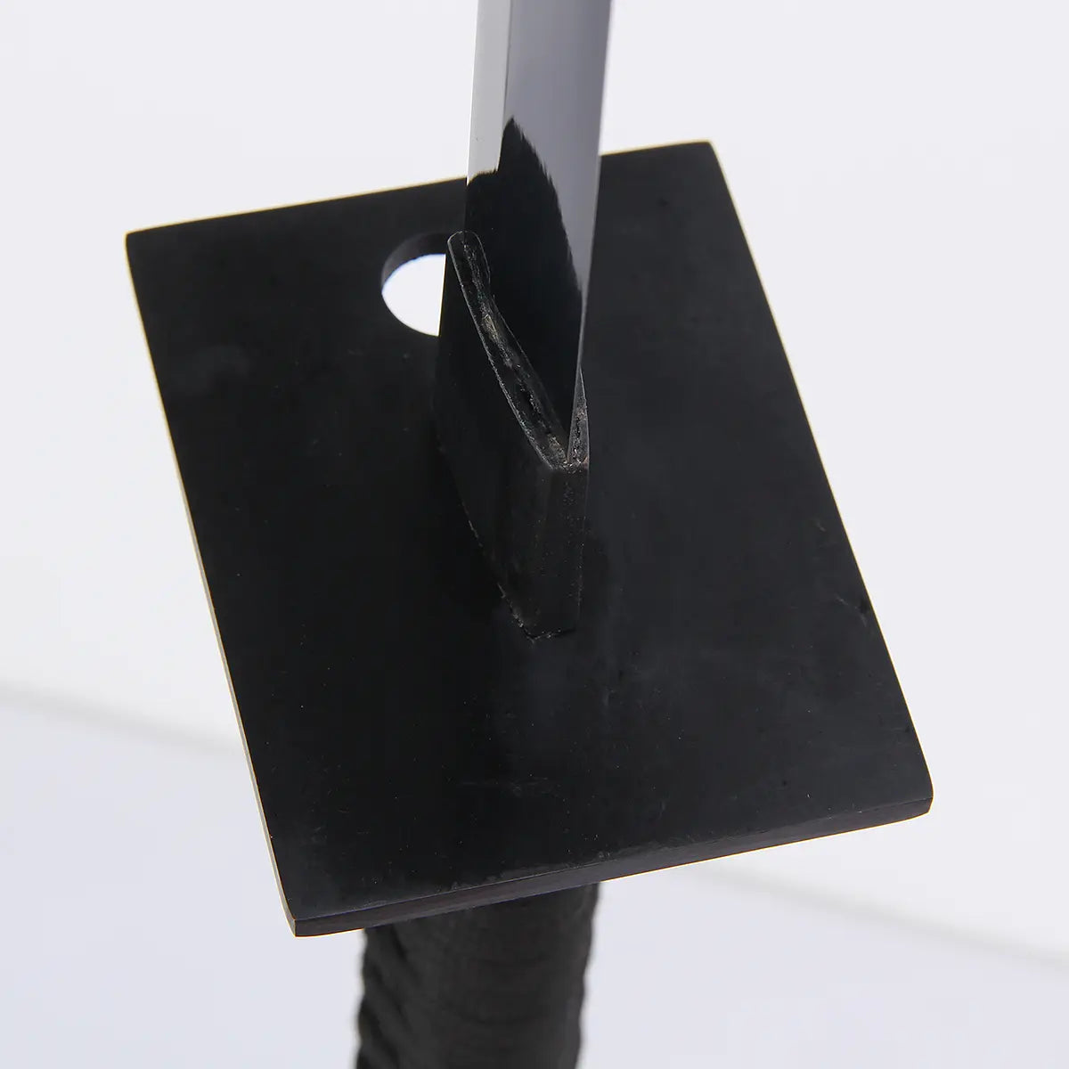 Gros plan minimaliste de la tsuba carrée noire du katana “Shinobi”, lame sombre passant au centre avec habaki visible, léger reflet métallique, fond blanc neutre — katana ninja, ninjatō, détail garde, Blade Bushido.