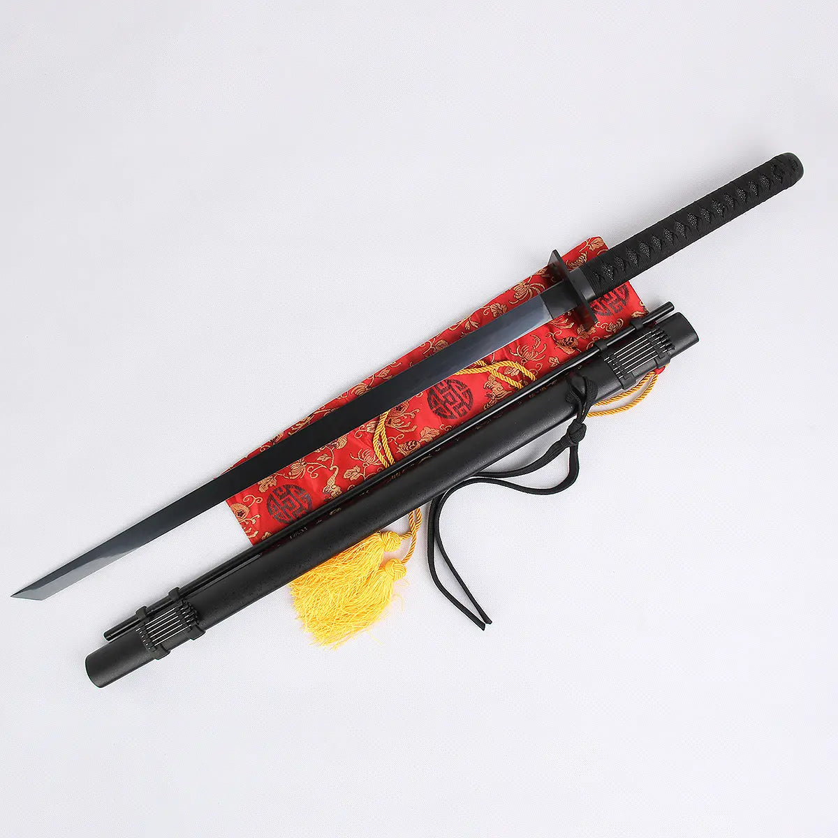 Katana japonais artisanal “Shinobi” dégainé sur fond blanc, lame noire tendue en diagonale au-dessus d’un sac en brocart rouge à pompon jaune, tsuba carrée, tsuka noire tressée, fourreau noir mat à côté avec porte-aiguilles décoratif — katana ninja, ninjatō, katana noir, Blade Bushido.
