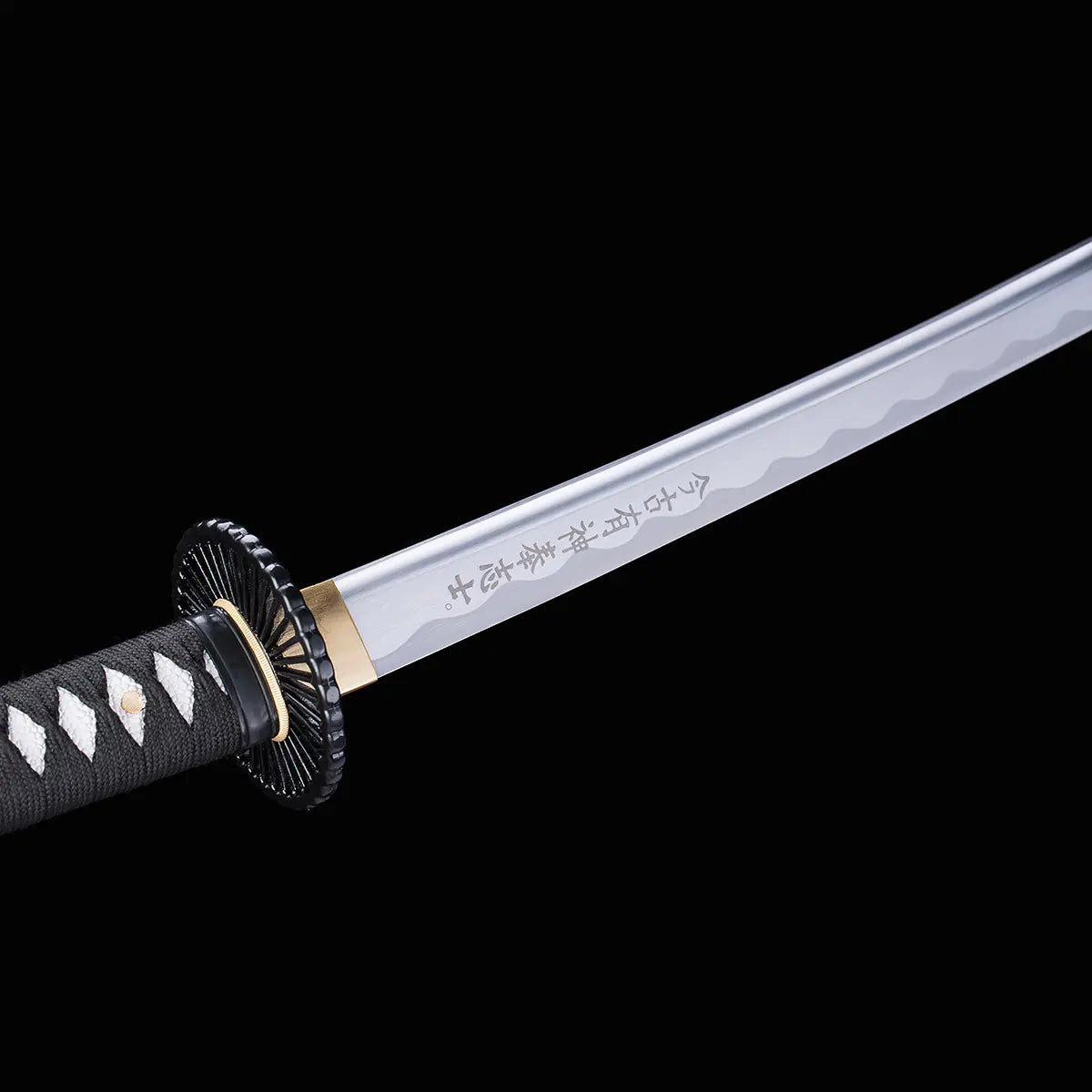 Détail de la lame gravée du katana japonais artisanal Shinshi no Ken sur fond noir, acier poli avec hamon ondulé visible, inscription japonaise le long de la lame, habaki doré, tsuba noire nervurée et manche noir avec tressage traditionnel laissant apparaître un samegawa blanc.
