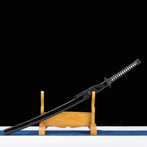 Katana japonais artisanal Shinshi no Ken présenté dans son fourreau noir laqué sur un support en bois sculpté de couleur dorée, fond noir profond avec base claire et tissu bleu, poignée noire avec tressage traditionnel et samegawa blanc visible, sageo gris foncé noué autour du saya.
