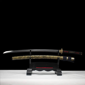 Katana japonais de combat Okinawa en acier T10, lame entière exposée sur support en bois noir, fourreau doré veiné noir, fond studio sombre.