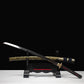 Katana japonais de combat Okinawa en acier T10, lame sortie du fourreau décoré, exposée sur support traditionnel, ambiance sombre.