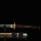 Gros plan de la poignée du katana japonais de combat Okinawa, tsuka noir tressé avec losanges rouges et ornements dorés, fond noir élégant.