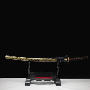Katana japonais de combat Okinawa dans son saya doré veiné noir, posé sur support en bois noir, fond studio minimaliste.