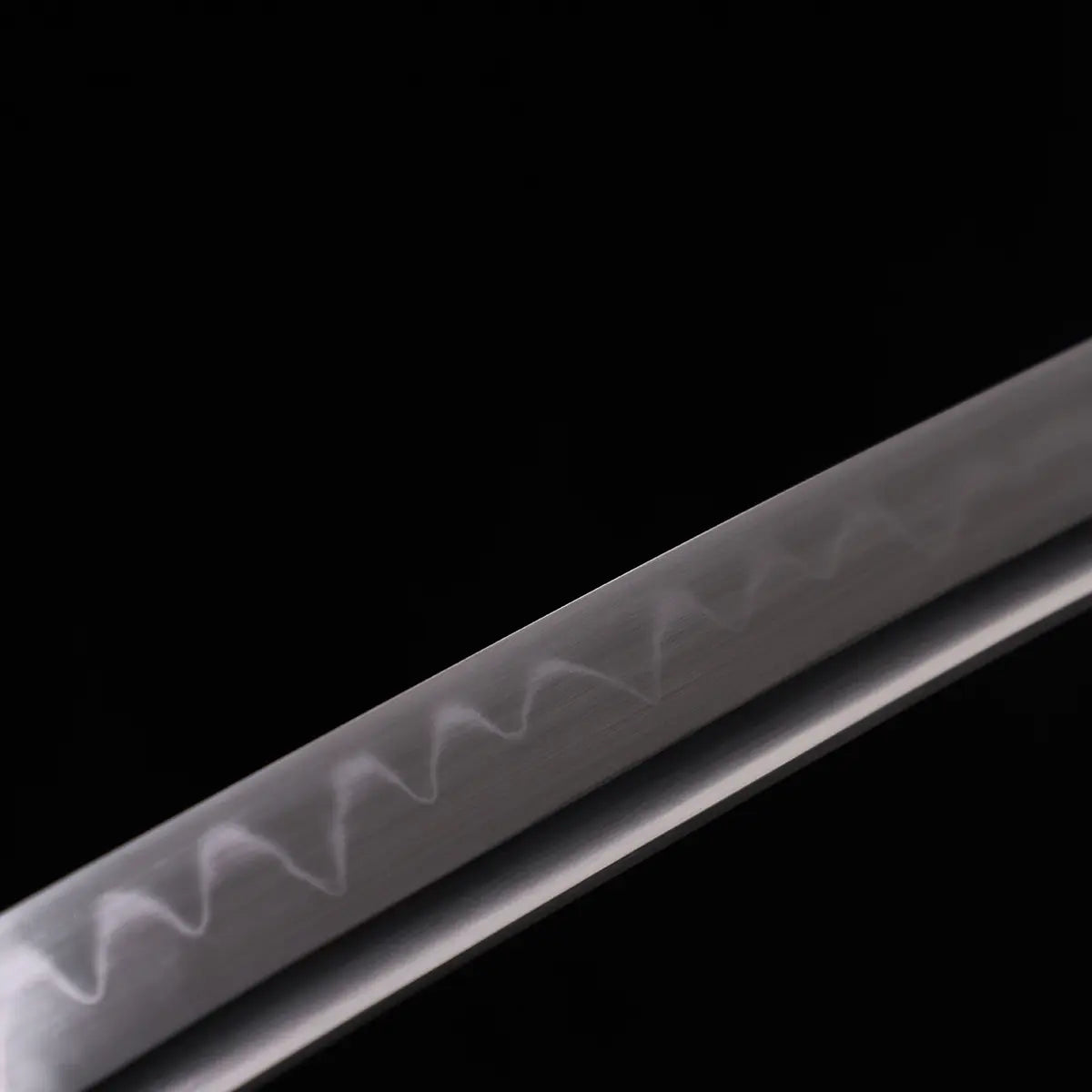 Gros plan sur la lame du katana japonais Kannon Ryū en acier 1045 trempé à l’argile, montrant un hamon ondulé authentique, capturé sur fond noir studio Blade Bushido.
