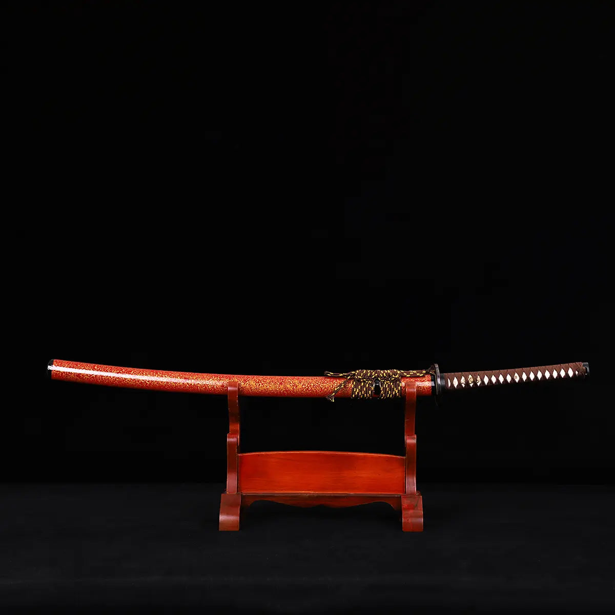 Katana japonais Kannon Ryū au fourreau rouge laqué moucheté or, posé sur un support en bois verni, sur fond noir studio. Sabre artisanal Blade Bushido à hamon authentique en acier 1045 trempé à l’argile.