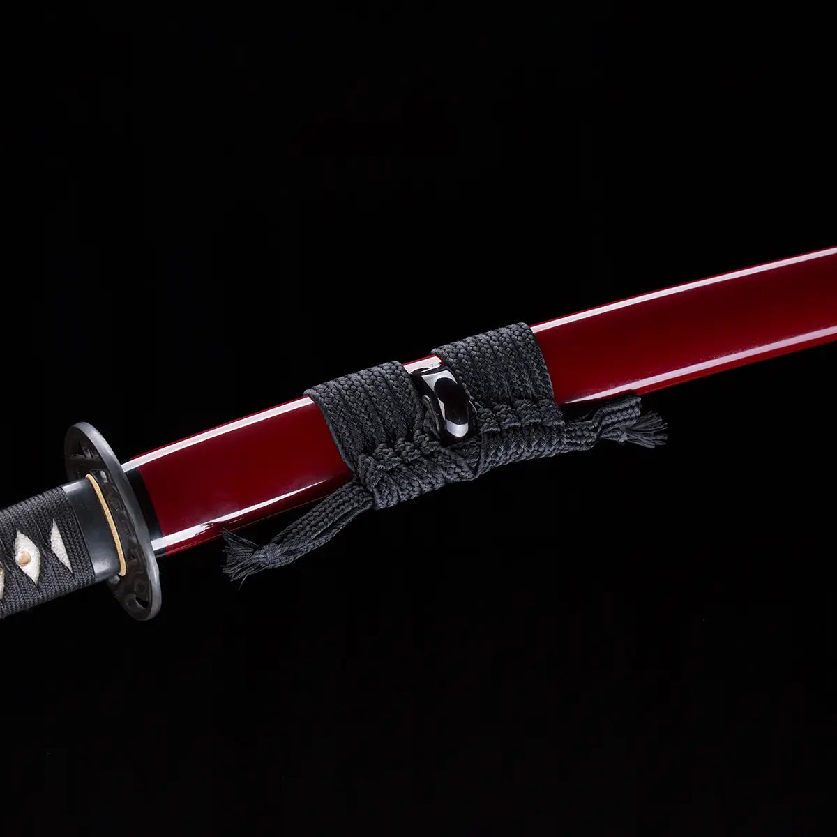 Détail du katana japonais “Kurenai no Tsuki” avec saya rouge laqué brillant, sageo noir soigneusement noué et garde tsuba partiellement visible, photographié sur fond noir studio – katana traditionnel Blade Bushido.