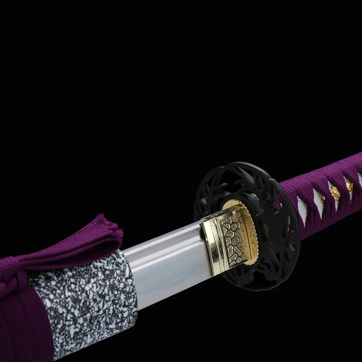 Gros plan du katana japonais Murasaki no Kage sur fond noir montrant la lame polie sortant du fourreau noir à éclaboussures blanches, habaki doré gravé, tsuba noire ajourée et poignée violette tressée avec peau de raie blanche visible.
