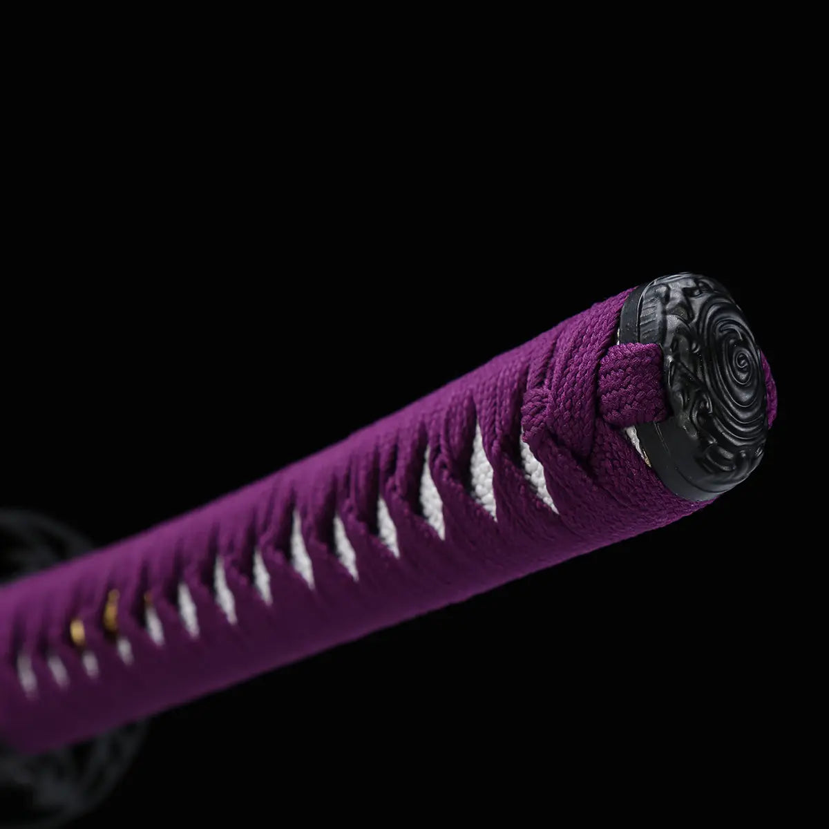 Détail de la poignée violette du katana japonais Murasaki no Kage photographiée sur fond noir, tsuka tressée laissant apparaître la peau de raie blanche, avec kashira noire sculptée visible à l’extrémité du manche.
