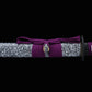 Gros plan du fourreau du katana japonais Murasaki no Kage sur fond noir, saya noir laqué avec motif d’éclaboussures blanches entouré d’un cordon sageo violet noué, avec la tsuba noire partiellement visible à
