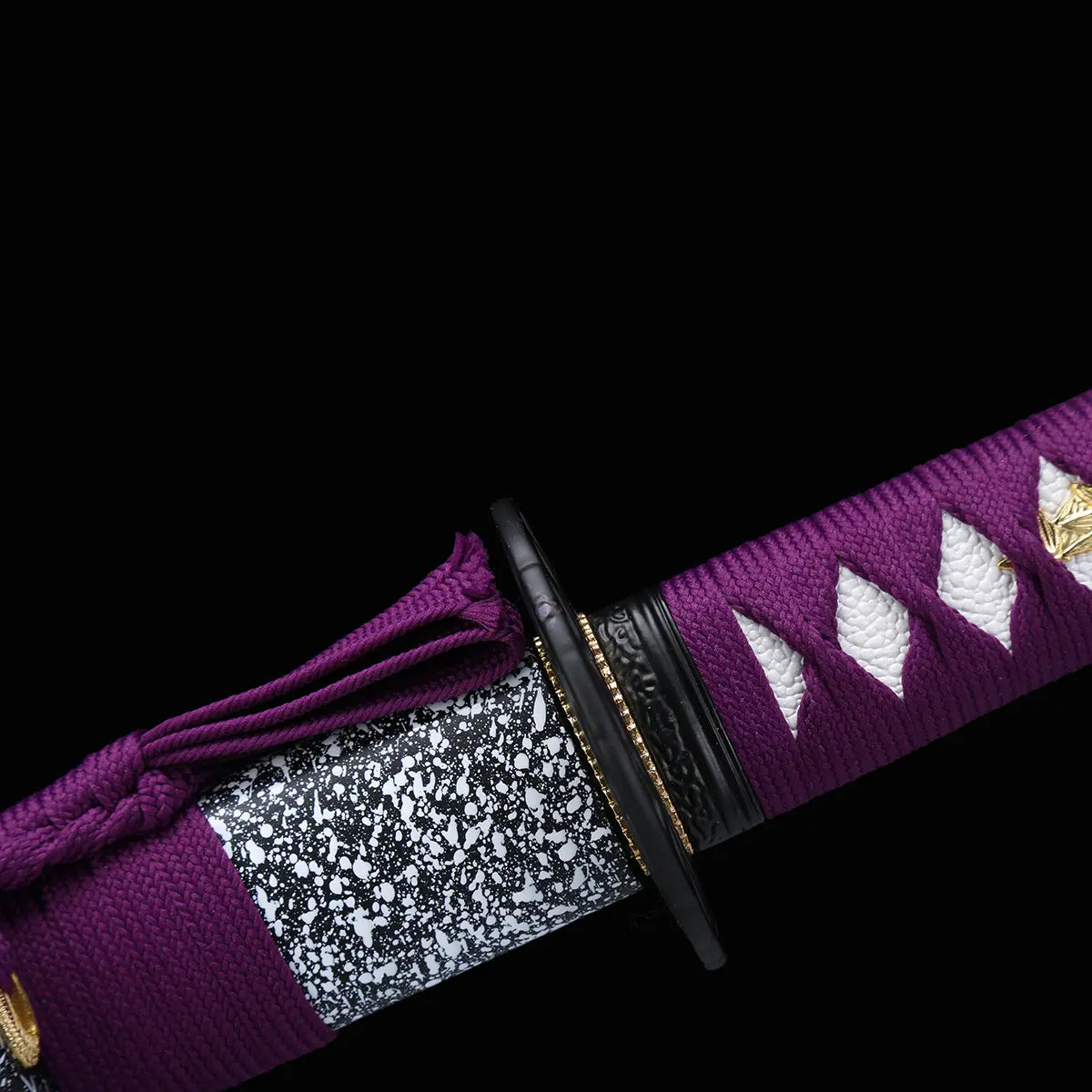 Gros plan du katana japonais Murasaki no Kage sur fond noir montrant la tsuba noire, le habaki doré, la poignée violette tressée avec peau de raie blanche et le fourreau noir laqué avec motif d’éclaboussures blanches, accompagné d’un cordon sageo vi
