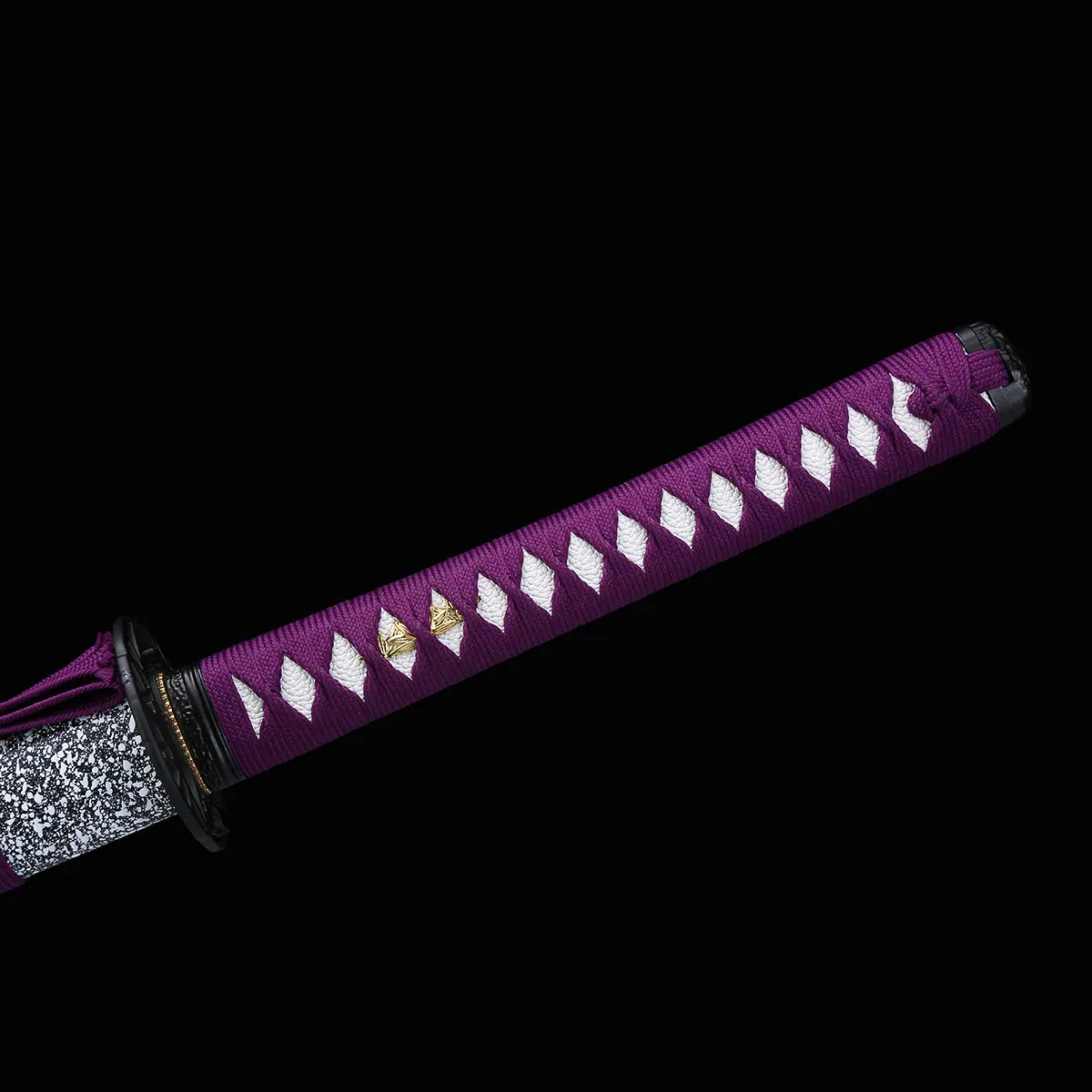 Détail du manche du katana japonais Murasaki no Kage sur fond noir, poignée violette tressée en losanges laissant apparaître la peau de raie blanche, menuki dorés visibles sous le tressage, avec la tsuba noire et le début du fourreau noir à éclaboussures blanches parti
