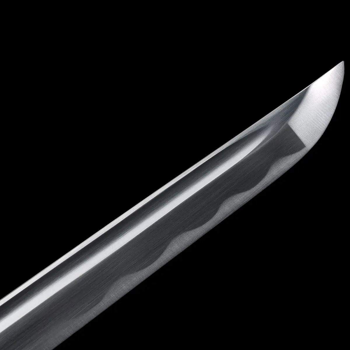 Gros plan sur la pointe du katana japonais Shirasaya en acier 1060, lame polie avec hamon ondulé visible.